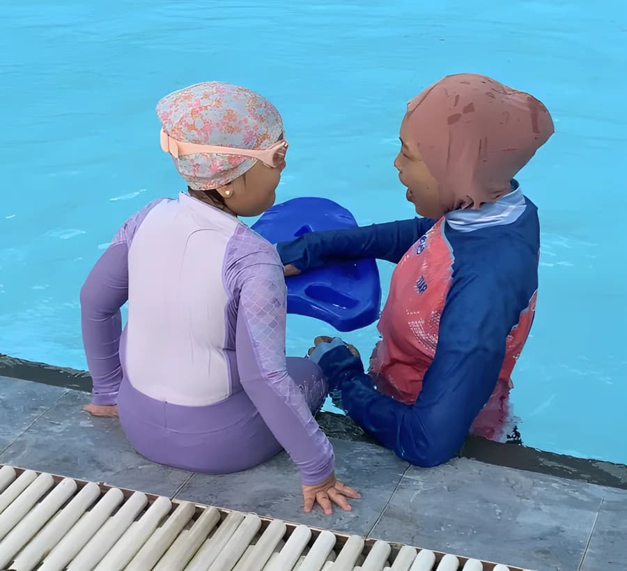 Anak dan pelatih beradaptasi di tepi kolam dengan papan renang